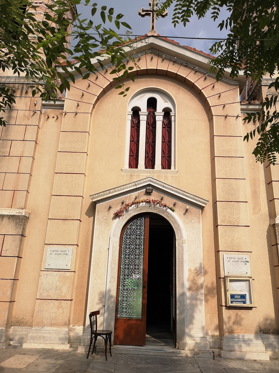 Simple exterior of Greek Orthodox Church with decorated window and cross on top
