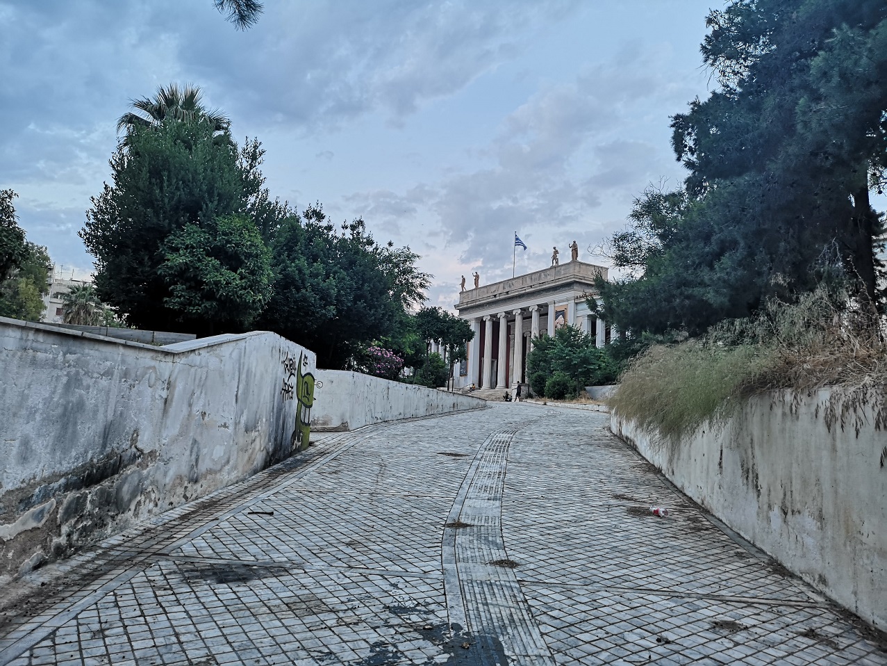The white Classical architecture of the National Archaeological Museum with trees on either side and the tiled driveway curving up,, Athens, Greece